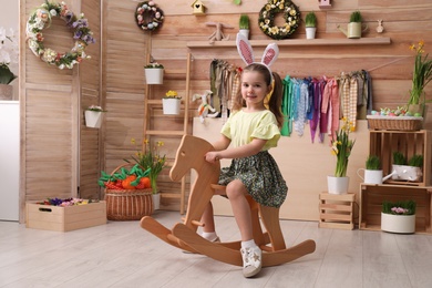 Photo of Adorable little girl with bunny ears on rocking horse in Easter photo zone