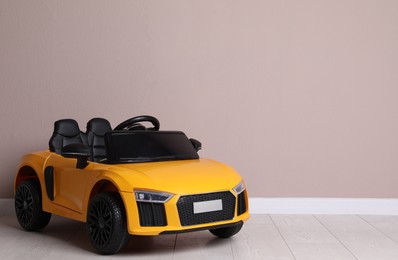 Child's electric toy car near beige wall indoors. Space for text