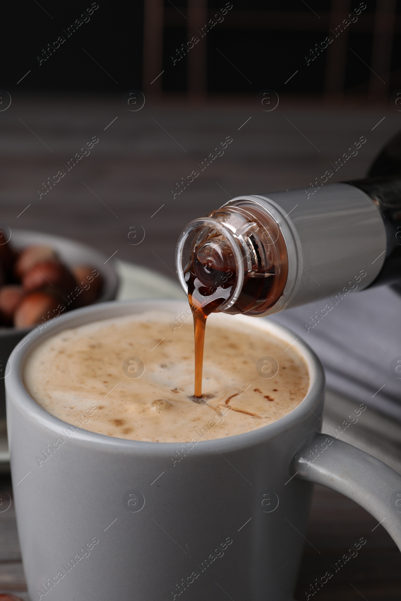 Photo of Pouring delicious hazelnut syrup into cup with coffee at table, closeup