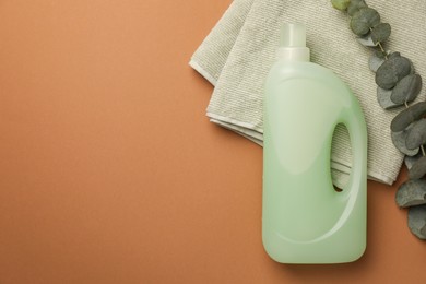Photo of Bottle of fabric softener, terry towels and eucalyptus branches on brown background, flat lay. Space for text