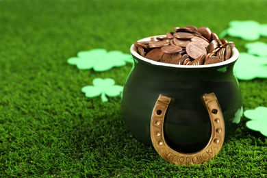 Photo of Pot of gold coins, horseshoe and clover leaves on green grass, space for text. St. Patrick's Day celebration