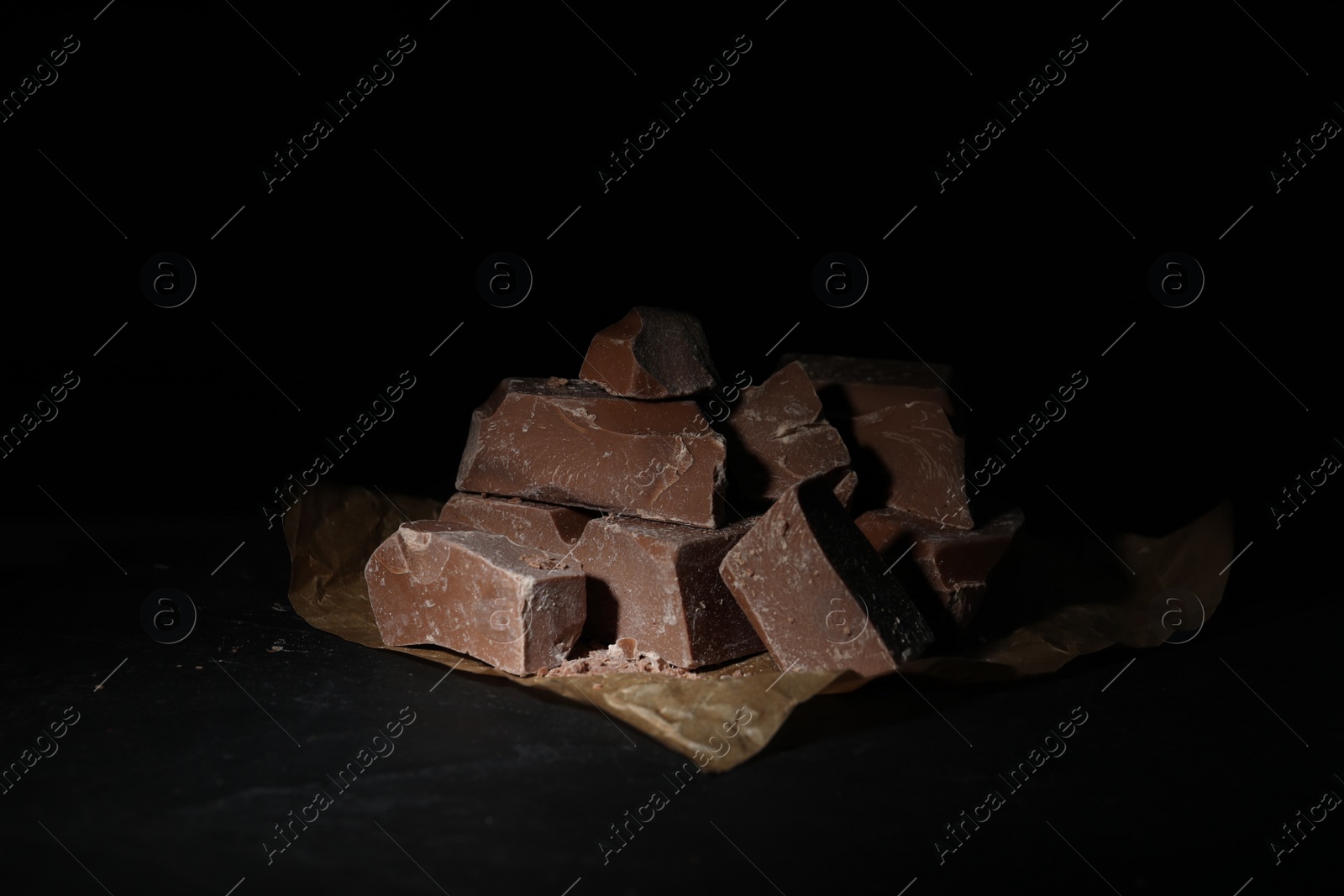 Photo of Pieces of tasty milk chocolate on black table, closeup