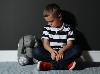 Photo of Sad little boy with toy near black wall. Domestic violence concept