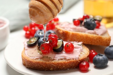 Photo of Tasty sandwiches with cream cheese, berries and honey, closeup