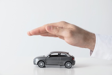 Photo of Male insurance agent covering toy car on white background, closeup