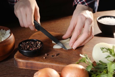Photo of Woman cutting ripe onion at wooden table, closeup
