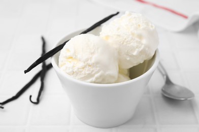 Photo of Delicious ice cream and vanilla pods on white tiled table, closeup
