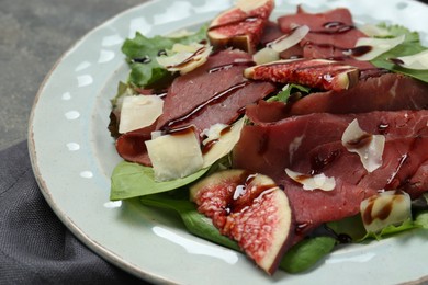 Photo of Plate with delicious bresaola salad on grey table, closeup