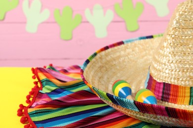 Photo of Mexican sombrero hat, poncho and maracas on yellow table, closeup. Space for text
