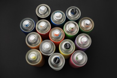 Cans of different graffiti spray paints on black background, above view
