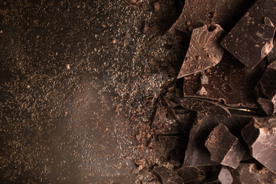 Photo of Pieces of dark chocolate on black table, flat lay. Space for text