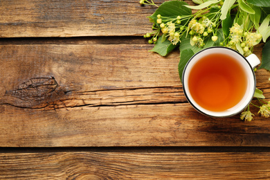 Photo of Cup of tea and linden blossom on wooden table, flat lay. Space for text