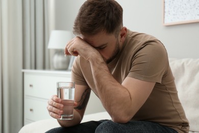 Photo of Man with glass of water and pill suffering from migraine at home