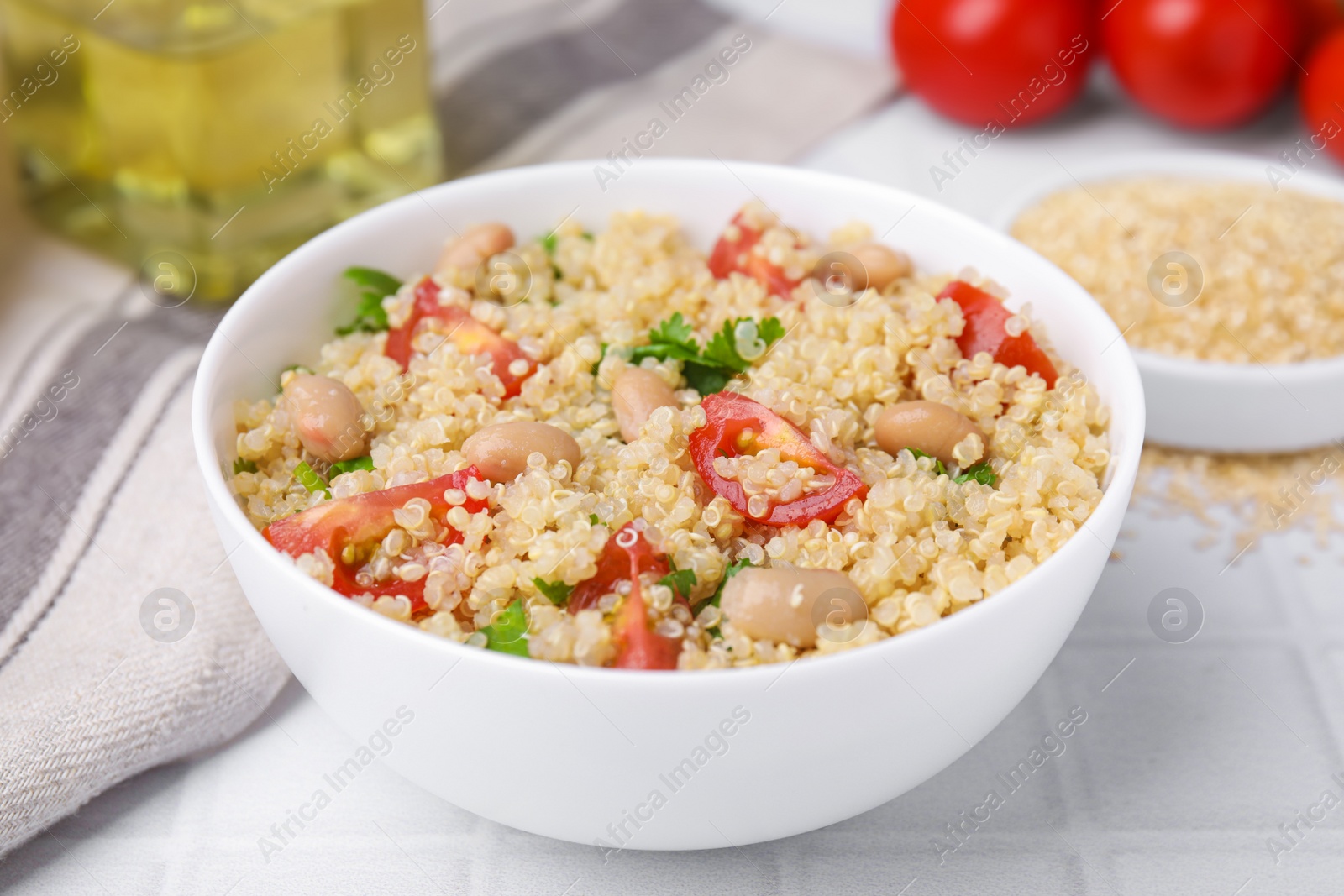 Photo of Delicious quinoa salad with tomatoes, beans and parsley served on white tiled table