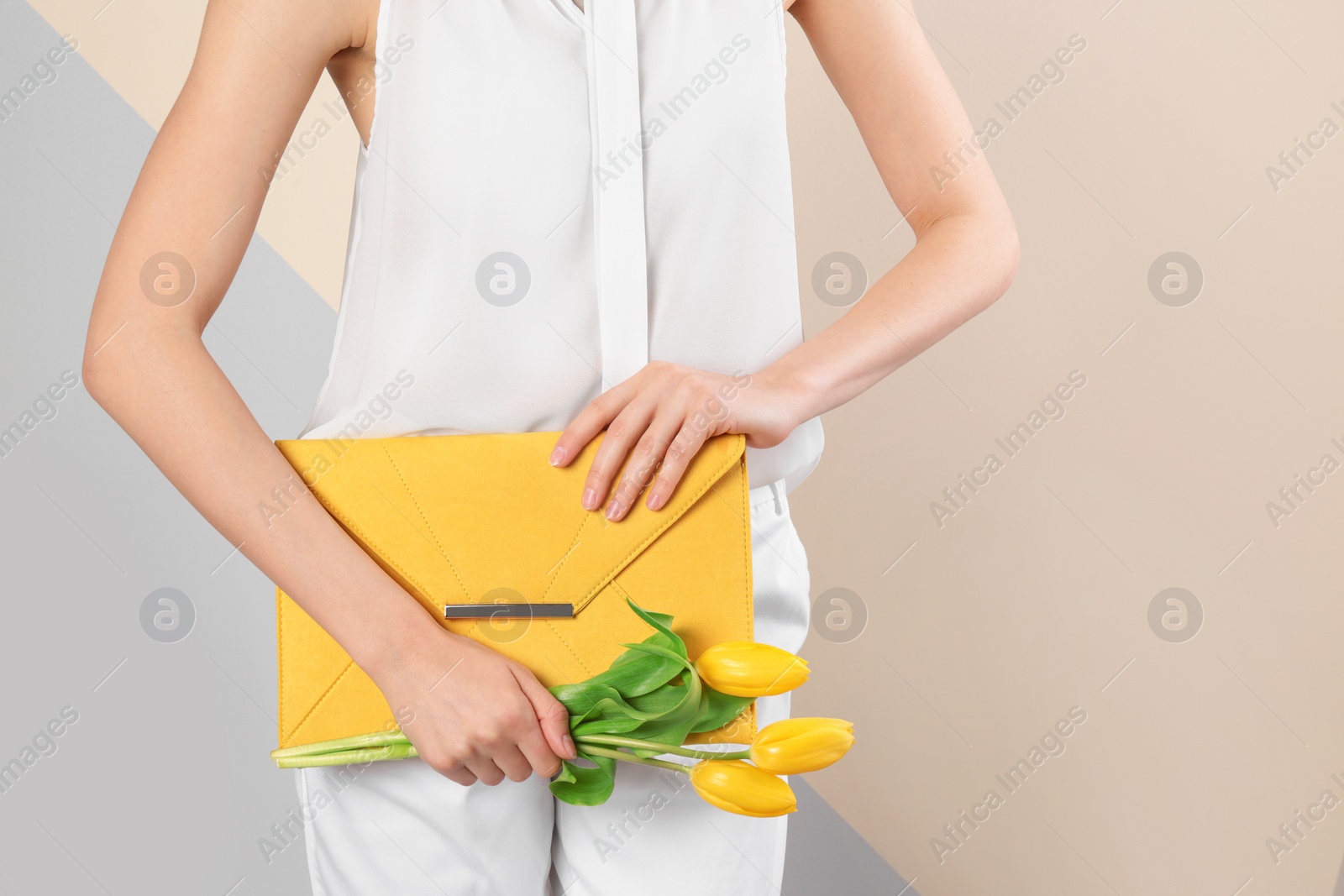 Photo of Stylish woman with clutch and spring flowers against color background, closeup