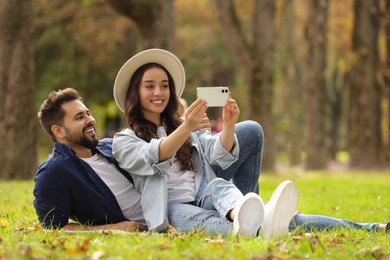 Beautiful young couple taking selfie in park. Space for text