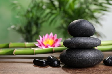Photo of Stacked spa stones, bamboo stems and flower on wooden table against blurred background. Space for text