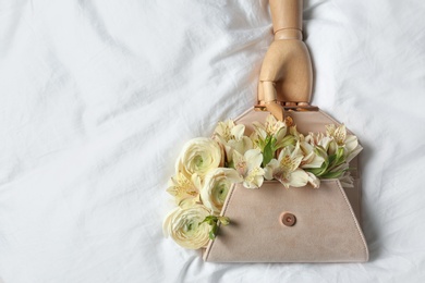 Photo of Stylish clutch with spring flowers and wooden mannequin hand on crumpled sheet, flat lay. Space for text