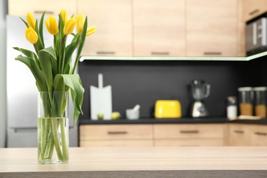 Photo of Glass vase with tulips on table in kitchen