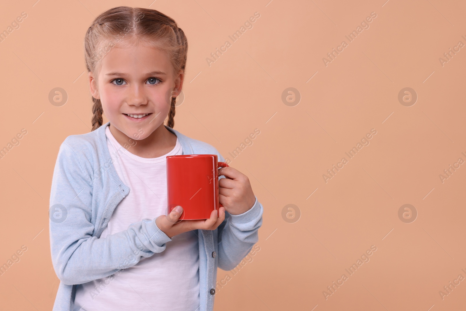 Photo of Happy girl with red ceramic mug on beige background, space for text