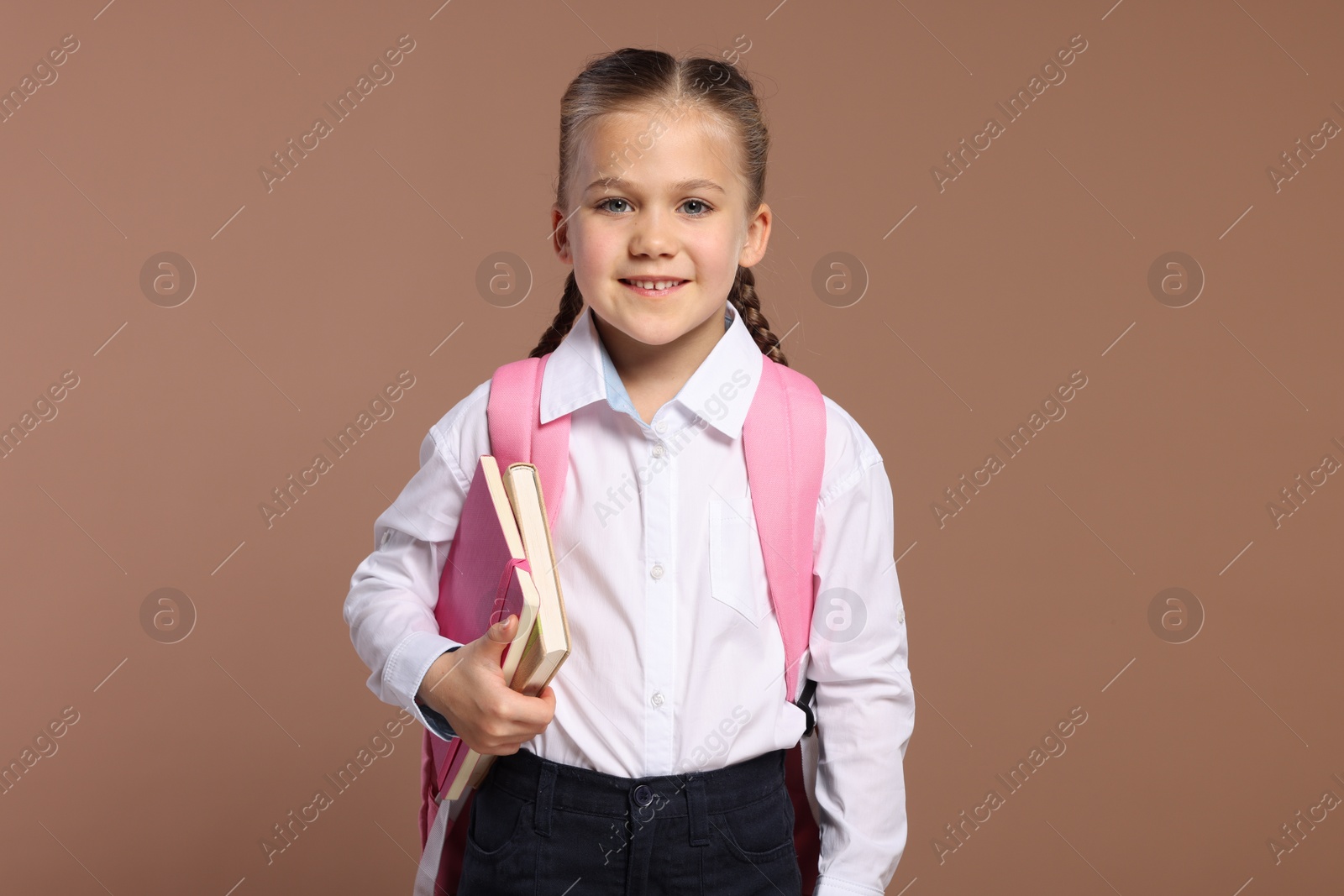 Photo of Happy schoolgirl with backpack and books on brown background