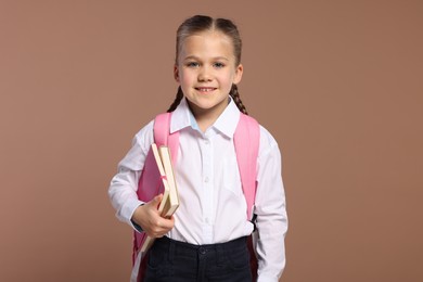 Happy schoolgirl with backpack and books on brown background