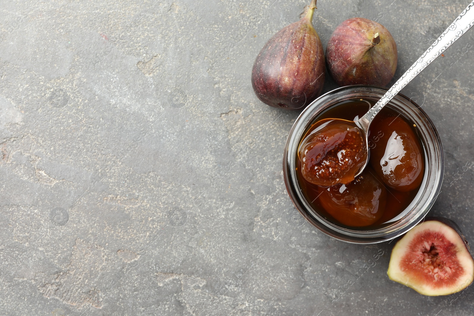 Photo of Jar of tasty sweet jam and fresh figs on grey table, flat lay. Space for text