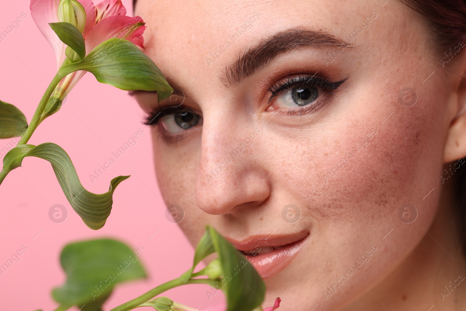 Photo of Beautiful woman with fake freckles and flower on pink background, closeup