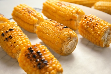 Photo of Fresh grilled tasty corn cobs on parchment paper, closeup