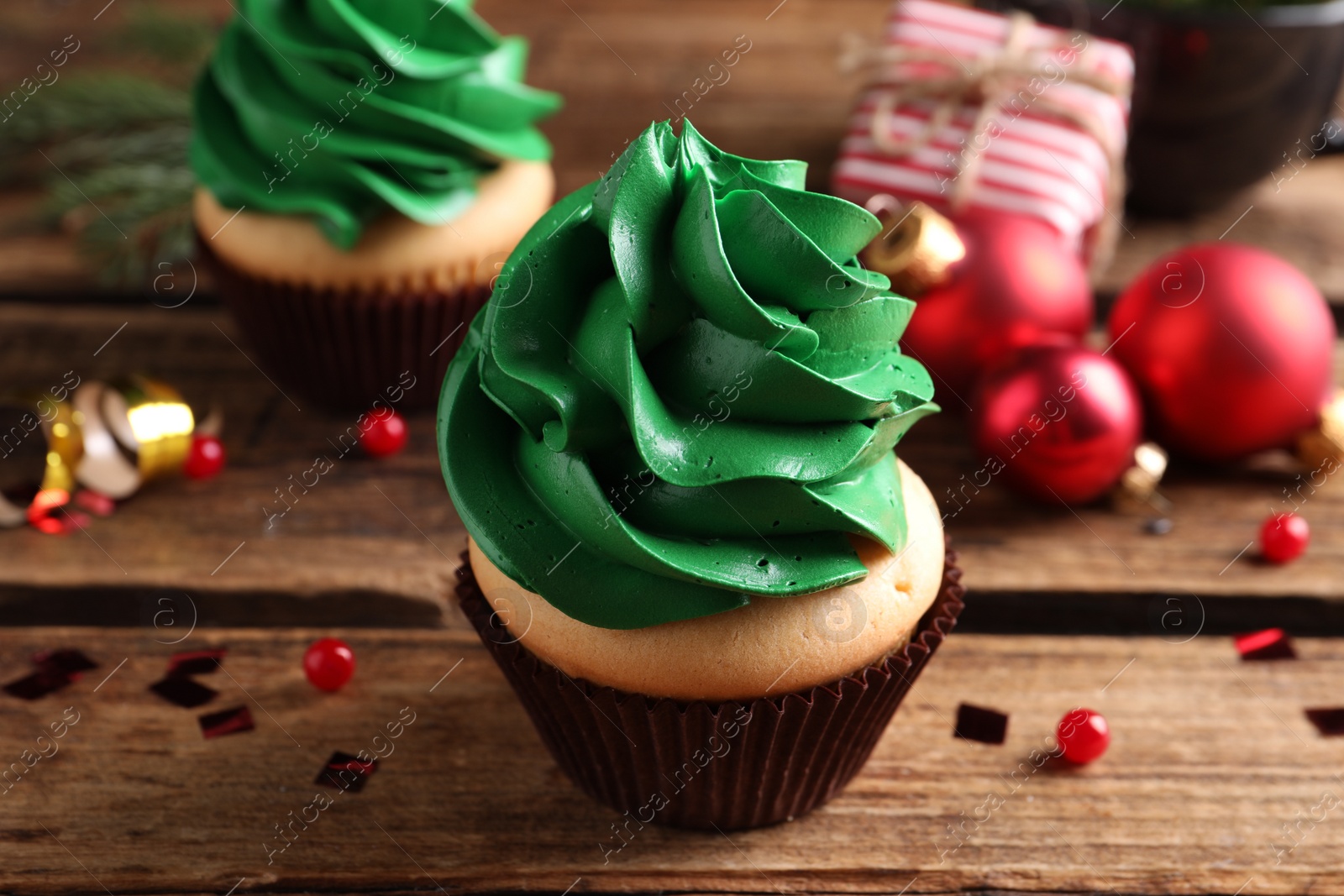 Photo of Delicious cupcake with green cream and Christmas decor on wooden table, closeup