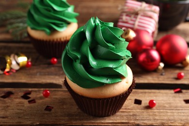 Delicious cupcake with green cream and Christmas decor on wooden table, closeup