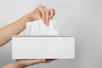 Woman taking paper tissue from holder on light background, closeup