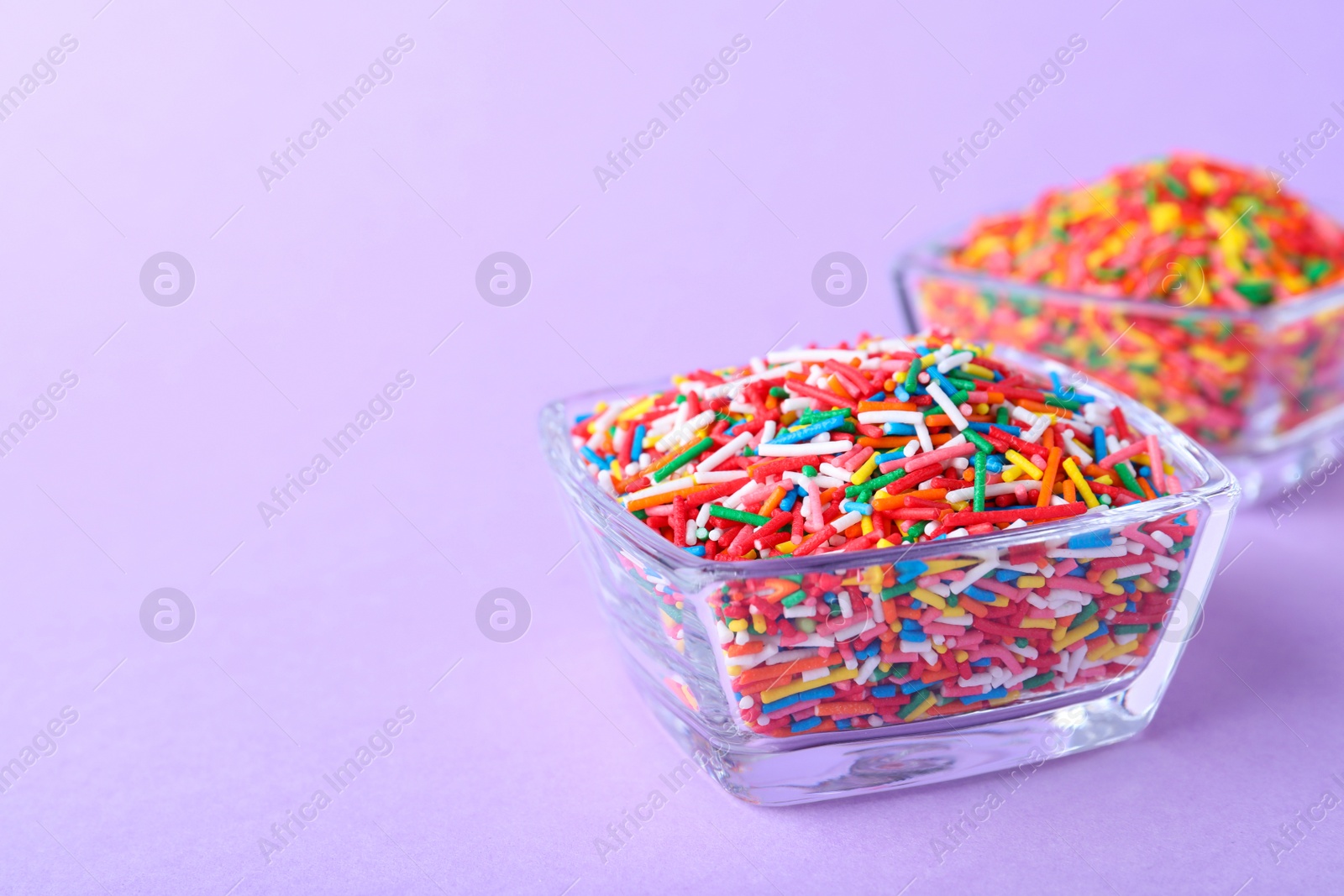 Photo of Colorful sprinkles in bowls on lilac background, space for text. Confectionery decor