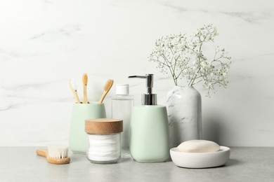 Different bath accessories, personal care products and gypsophila flowers in vase on gray table near white marble wall