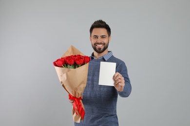 Happy man with red tulip bouquet and greeting card on light grey background. 8th of March celebration