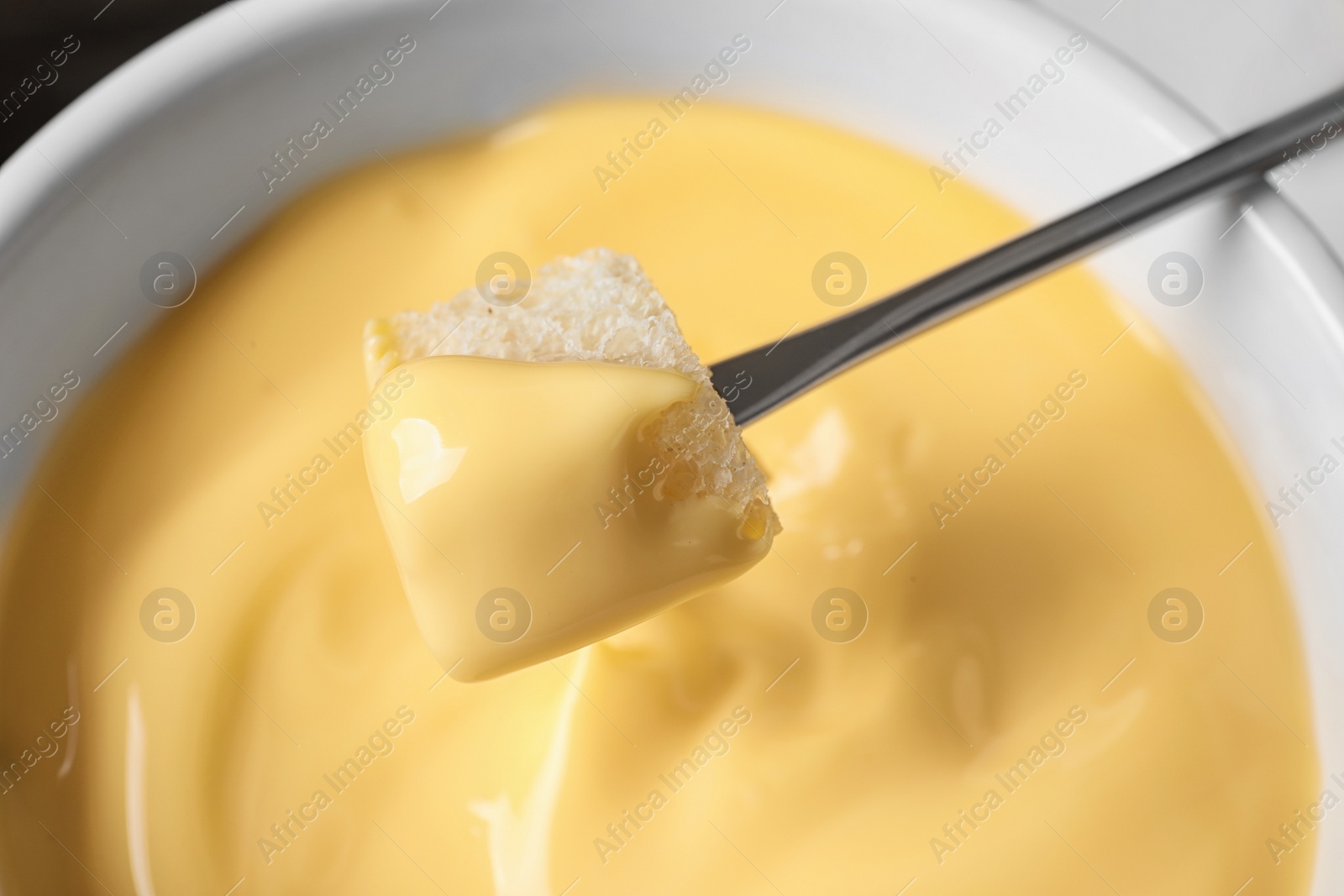 Photo of Dipping bread into tasty cheese fondue, closeup