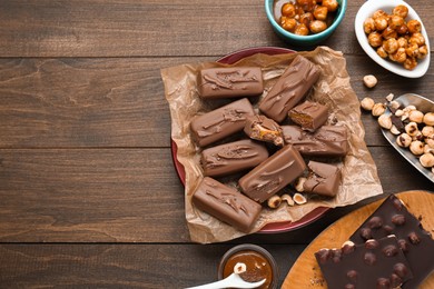 Photo of Delicious chocolate candy bars and nuts on wooden table, flat lay. Space for text