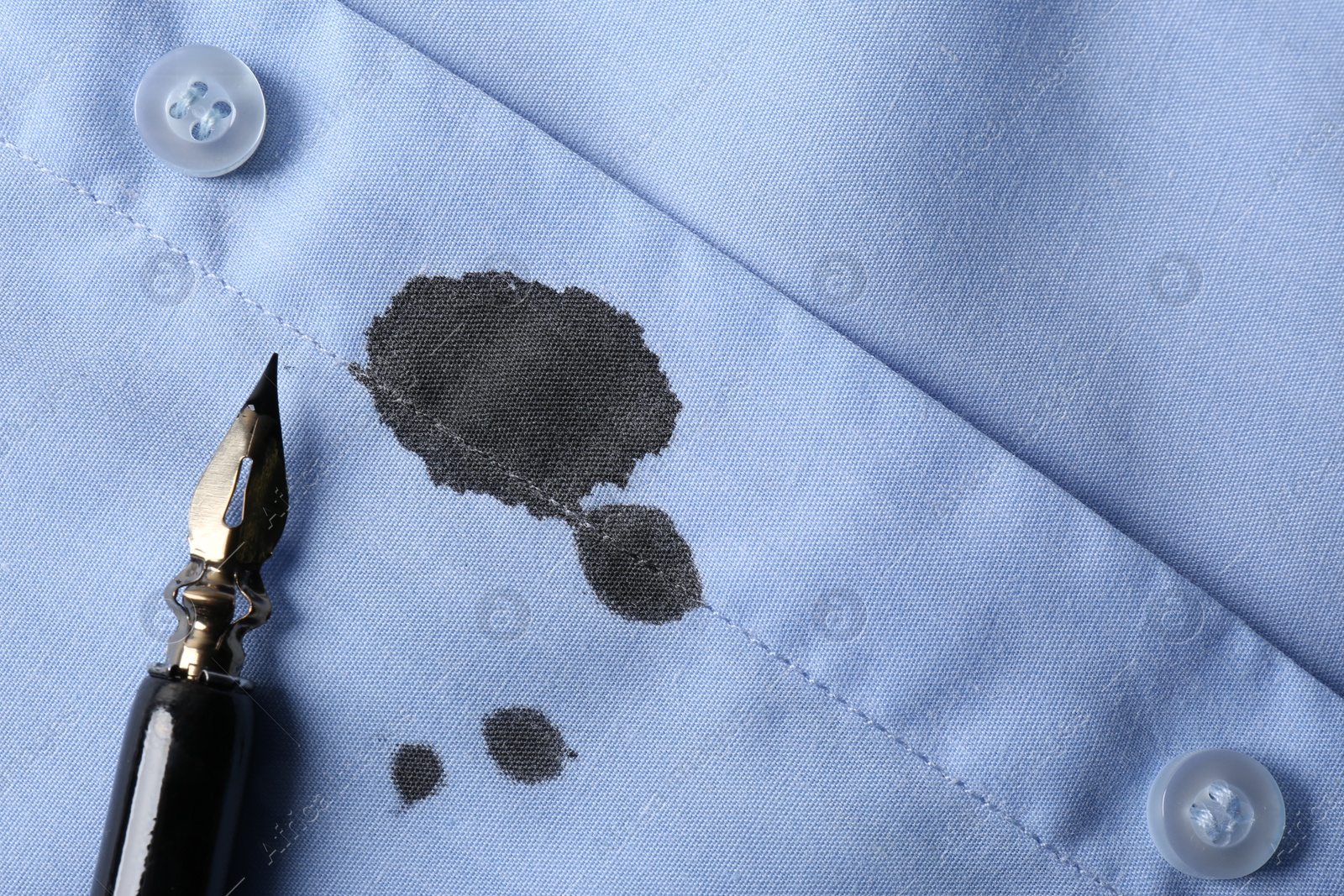 Photo of Black ink stain on light blue shirt and pen, top view. Space for text