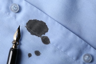 Black ink stain on light blue shirt and pen, top view. Space for text