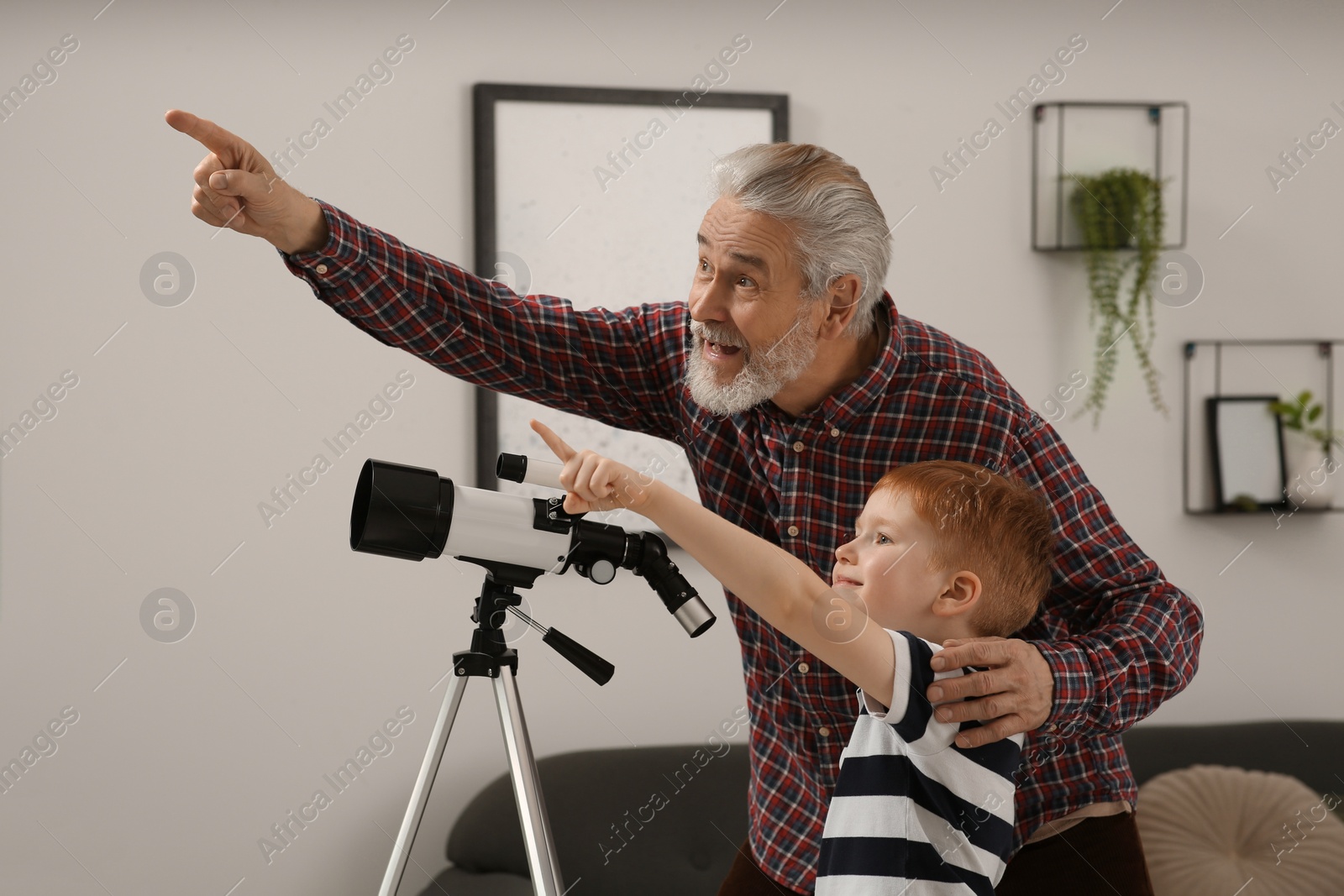 Photo of Little boy with his grandfather pointing at something near telescope in room