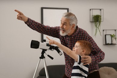 Little boy with his grandfather pointing at something near telescope in room