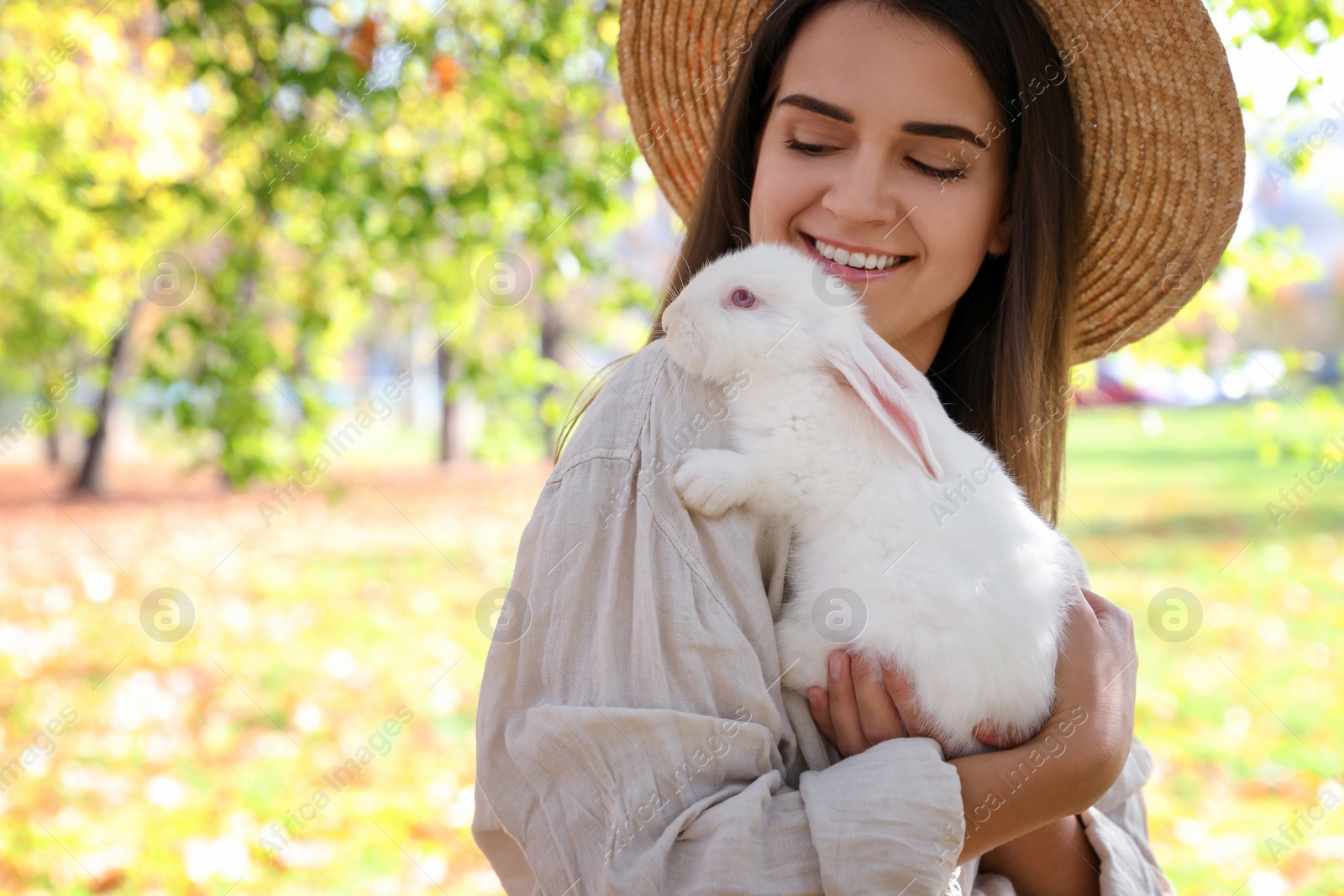 Photo of Happy woman holding cute white rabbit in park, space for text