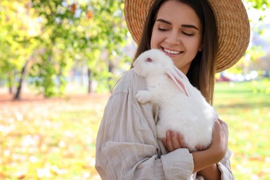 Photo of Happy woman holding cute white rabbit in park, space for text