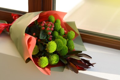 Bouquet of beautiful flowers wrapped in paper on window sill indoors