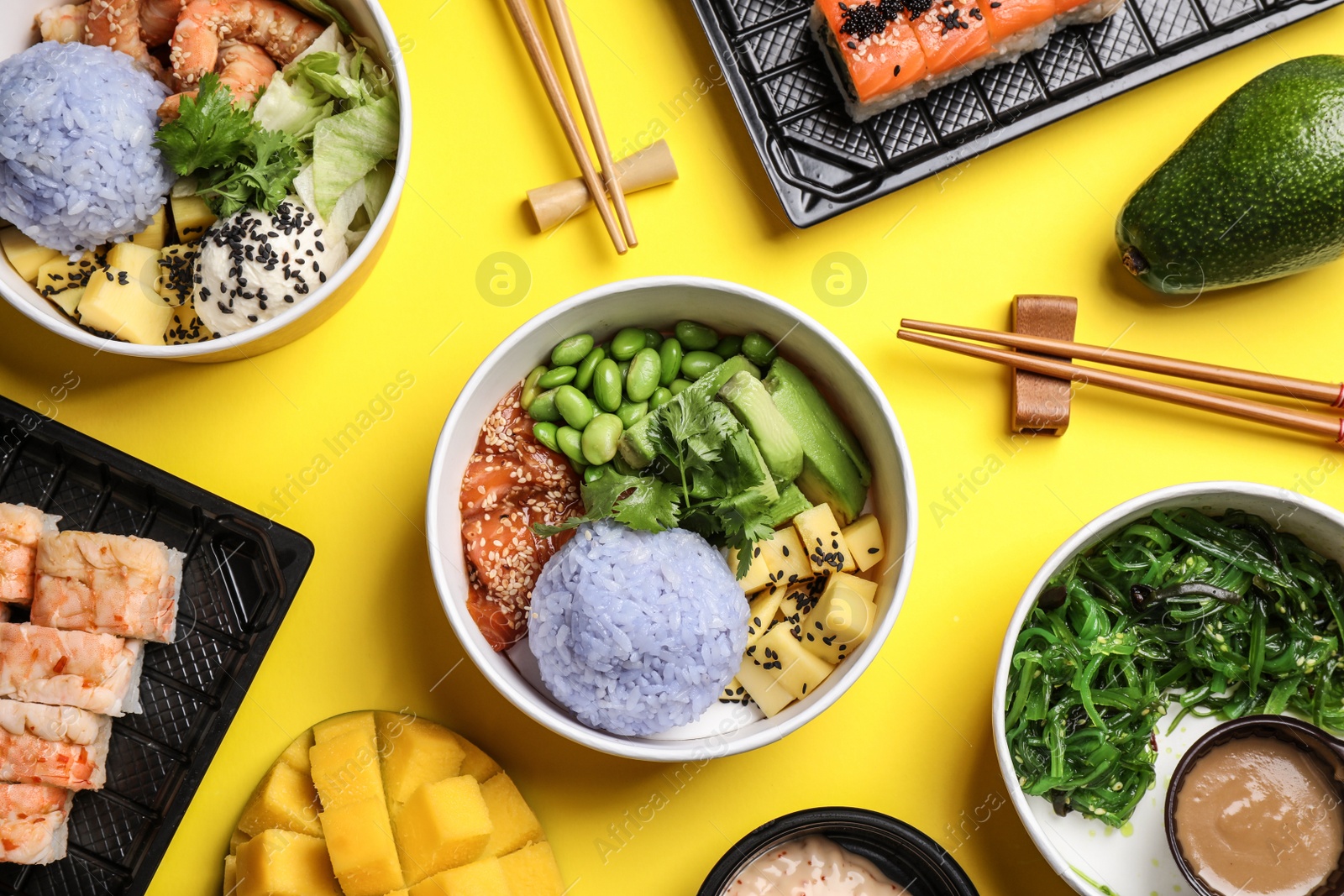 Photo of Delicious sushi rolls and poke bowls on yellow background, flat lay