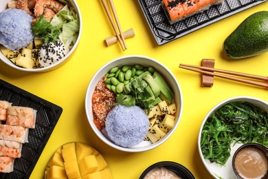 Delicious sushi rolls and poke bowls on yellow background, flat lay
