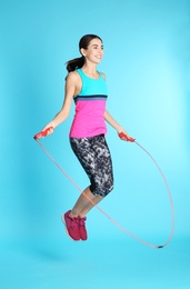 Photo of Full length portrait of young sportive woman training with jump rope on color background