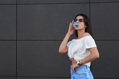 Photo of Beautiful woman blowing gum near dark tiled wall outdoors, space for text