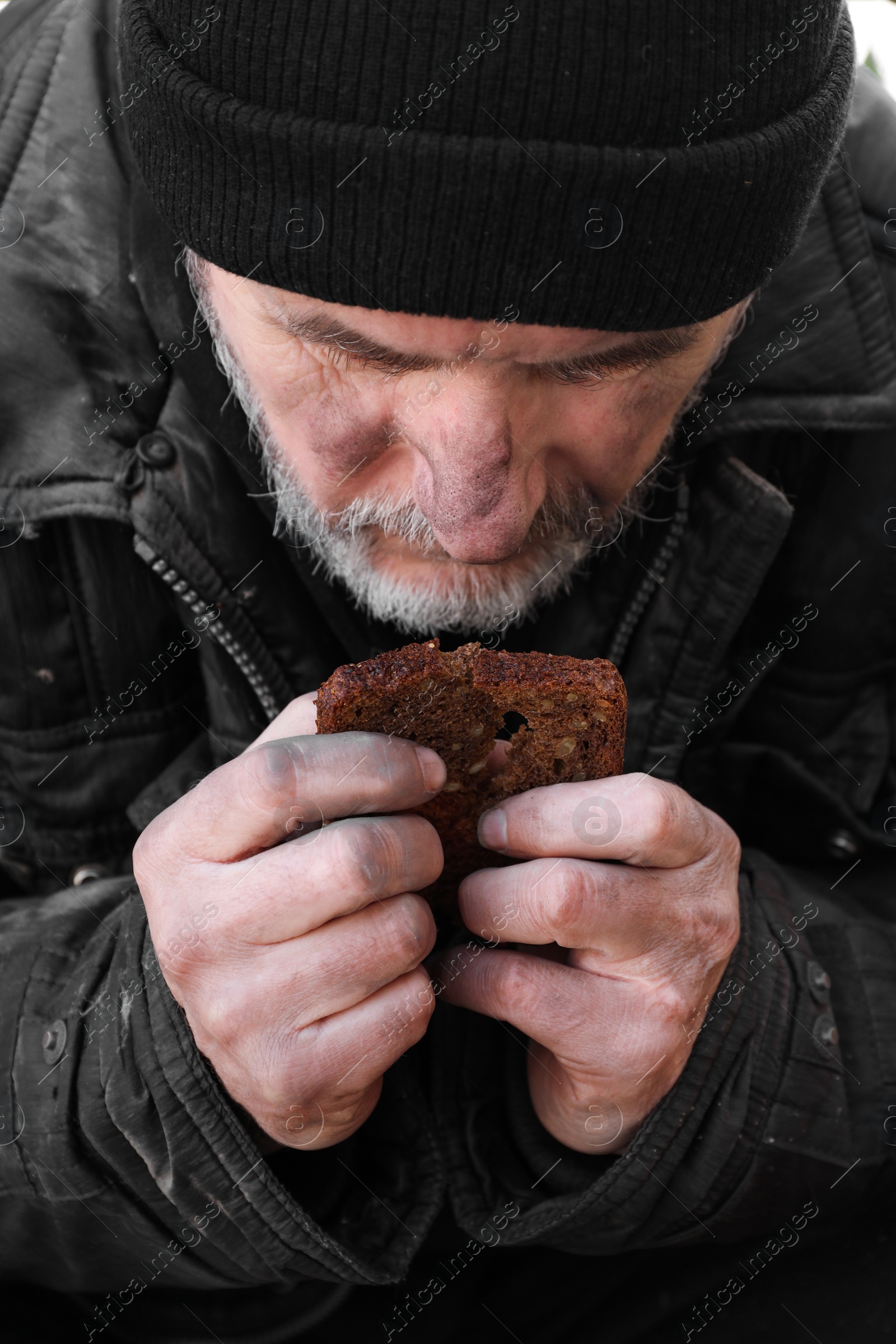 Photo of Poor homeless man holding piece of bread outdoors