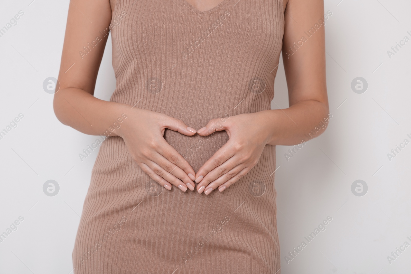 Photo of Pregnant woman in beige dress making heart with hands on white background, closeup